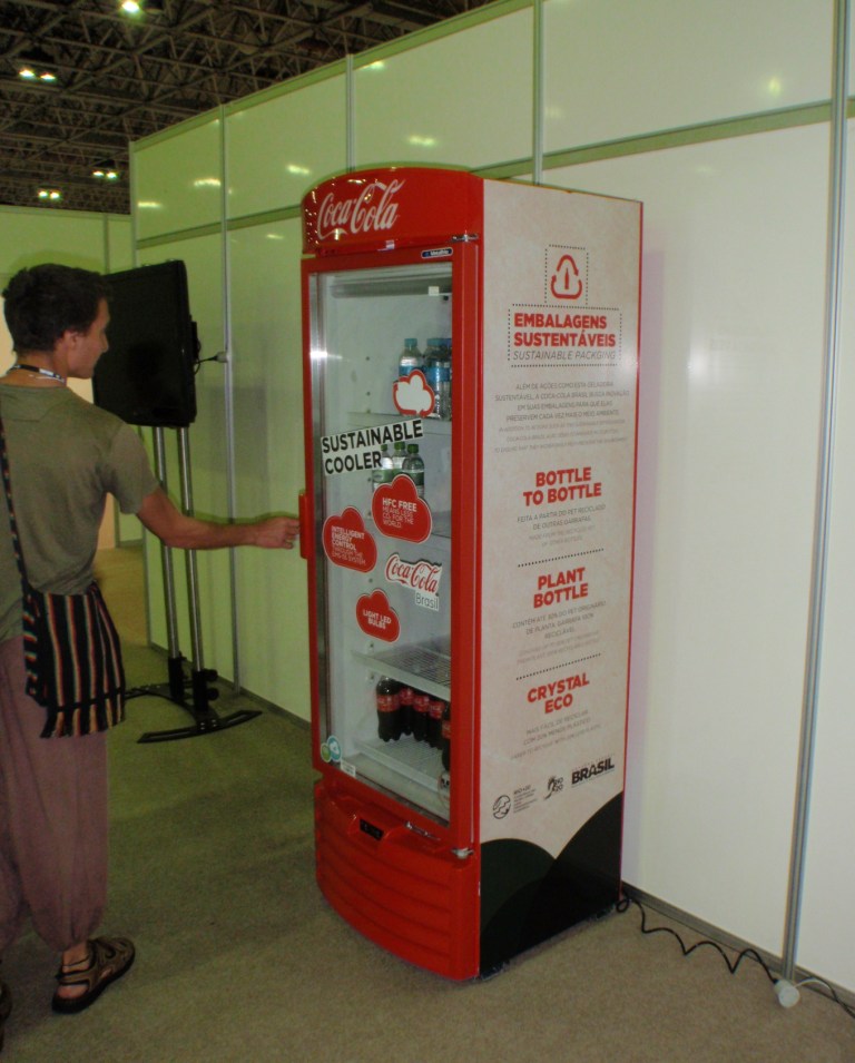 Grønne grønne og socialt bevidste coca cola er selvoeligelig til stede paa konference. I deres uendelige godhed har de stillet gratis drikkevarer til raadighed for stammefolk, NGO'er, statsoverhoveder og andre let paavirkelige.  Skiltet fortaeller om baeredygtiegt koeleskab, hele 5%groen flaske, kun x liter vand til at lave en hel cola osv osv. Sender en kaelig tanke til de landsbyer jeg har besoegt i Indien og Mexico som maa koebe Coca Colas kildevand fordi selv samme firma har pumpet grundvandet op saa landsbyen er tør. Store oliestater som Emiraterne og Kuwait har de stoerste stande der - og store skilte med deres baeredygtige byer. Sjovt for jeg synes at huske Dubai som det mindst baeredygtige samfund i verden - diktatur, minus rettigheder for de 90% immigranter etc etc.